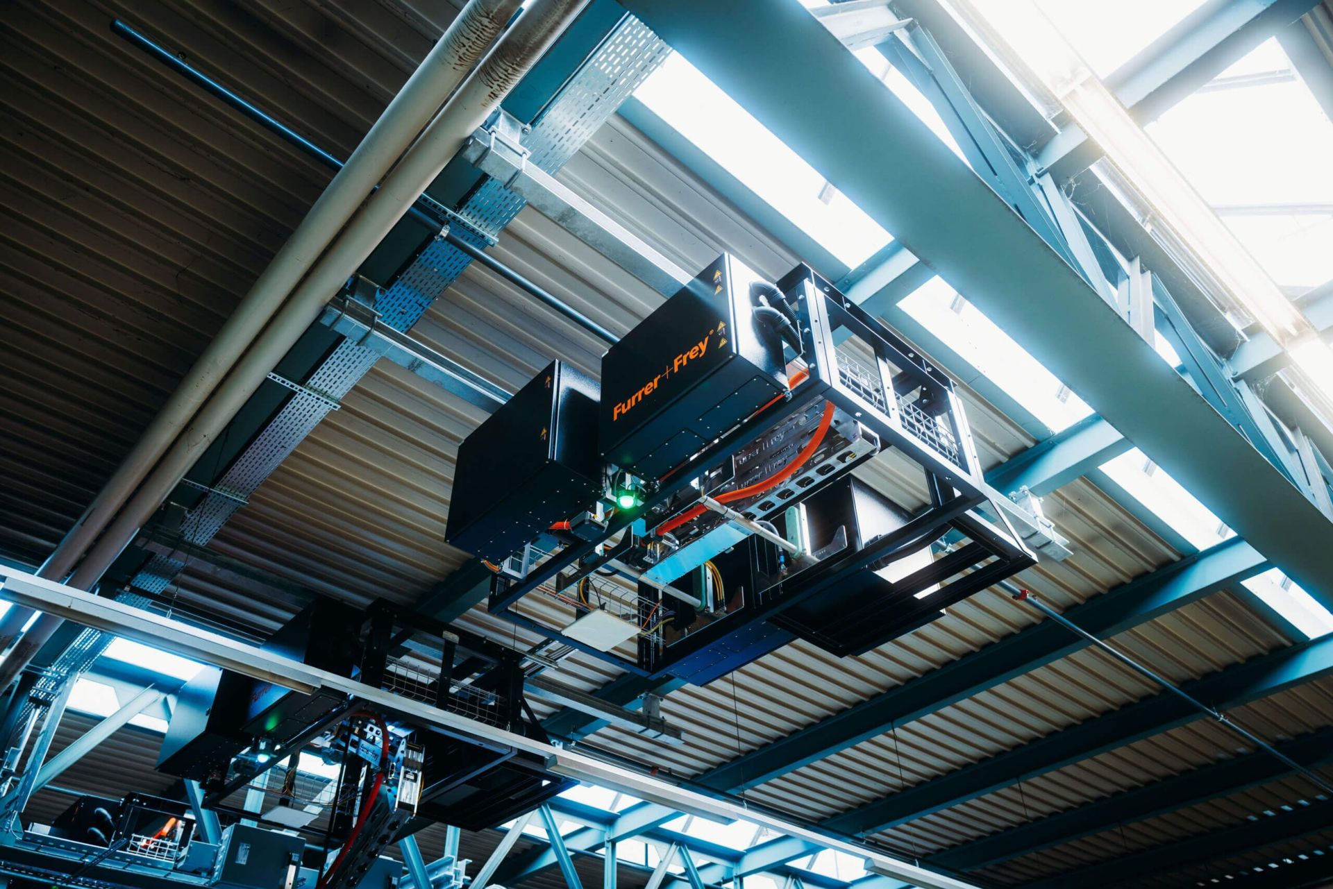 Ein robotergestütztes Lagersystem mit von der Decke hängenden Maschinen und Geräten, das zur automatischen Lagerung und Abfrage verwendet wird. Das System umfasst Metallrahmen, Förderbänder und verschiedene mechanische Komponenten, die für eine effiziente Bestandsverwaltung konzipiert sind.