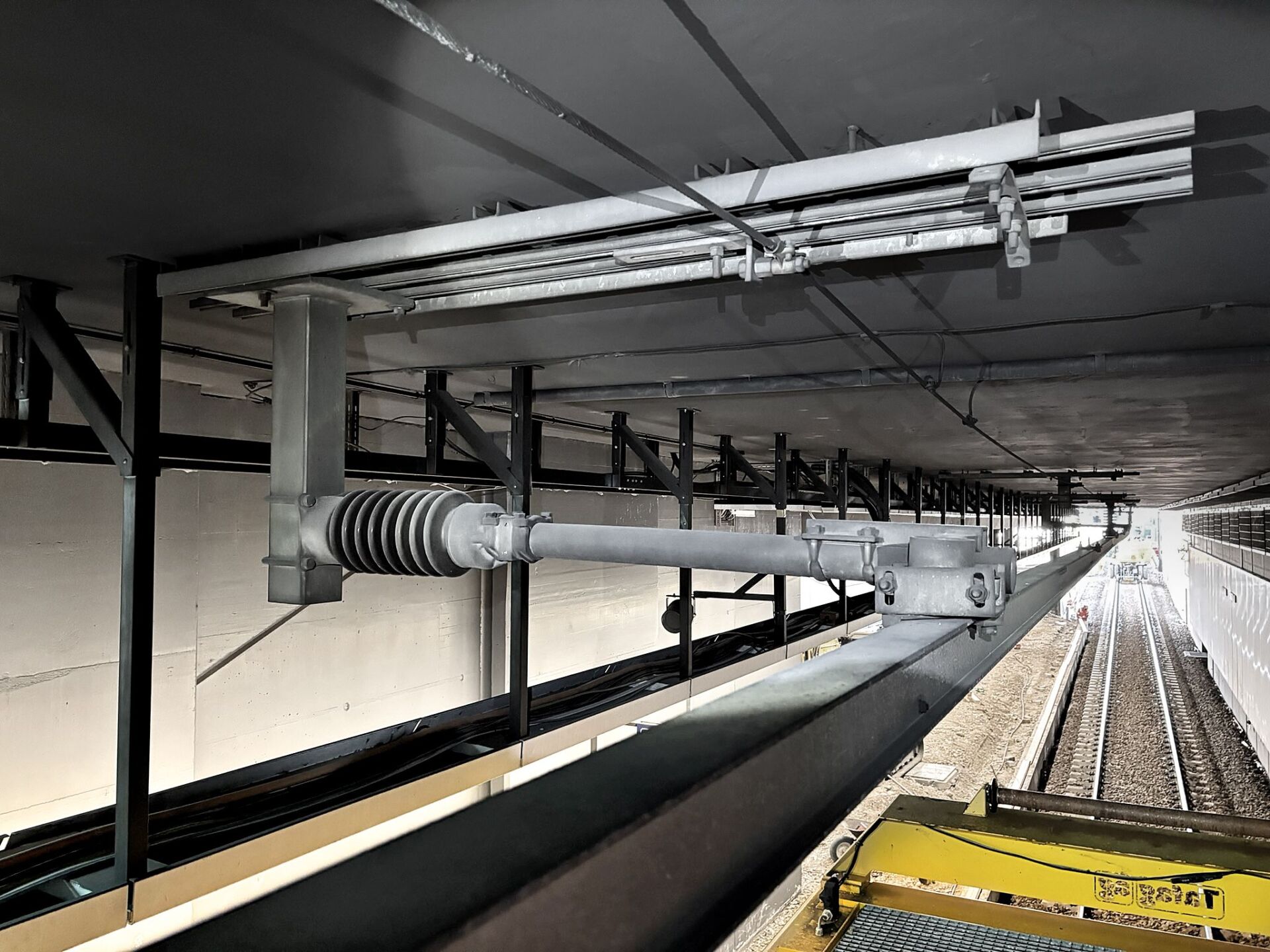 Unter einer Decke über den Gleisen im Bahnhof Opfikon ist die Deckenstromschiene 1. Generation angebracht, wobei die Gleise und die Ausrüstung darunter sichtbar sind.